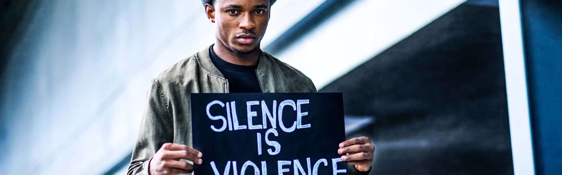 kr8tive media: african guy holding a black slate with silence is violence inscription